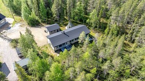 A modern two-story house surrounded by dense forest, with a gravel driveway and a small detached garage. - Villa Hellitä | Peaceful 3BR Villa with Hot Tub (Ylläsjärvi)