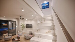 Ein modernes Interieur mit einer Marmortreppe, einer Sitzecke mit Couchtisch und einem an der Wand befestigten Fernseher.