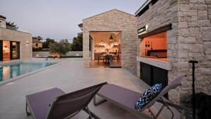 Ein modernes Haus mit Natursteinaußenwand, einem Schwimmbecken und einem Essbereich, der durch einen offenen Durchgang sichtbar ist.