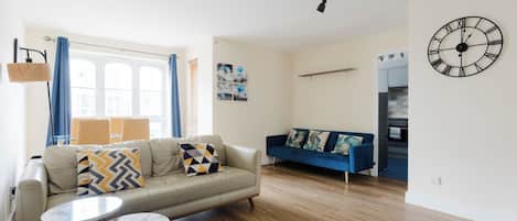 A modern living room with a sofa, two side tables, a patterned rug, and a wall clock.