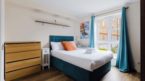 Ein Schlafzimmer mit einem Bett, einem Holzschrank, einem Nachttisch, einem Fenster mit Vorhängen und einem Bild an der Wand.