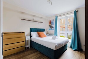 Ein Schlafzimmer mit einem Bett, einem Holzschrank, einem Nachttisch, einem Fenster mit Vorhängen und einem Bild an der Wand.