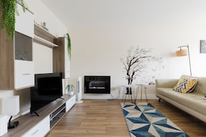 Ein modernes Wohnzimmer mit Flachbildfernseher, einer Couch, einem Couchtisch und einer Wandmalerei eines Baumes.