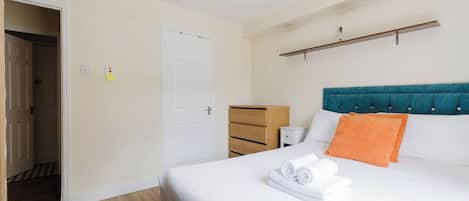A hotel room with a bed, a bedside table, a nightstand, a wardrobe, and a door.