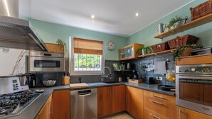 A modern kitchen with stainless steel appliances, wooden cabinets, and a window with blinds.
