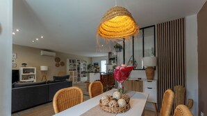 A dining area with a white table, wicker chairs, a woven light fixture, and a vase with flowers.