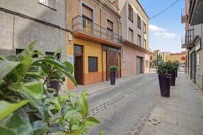 Une rue étroite, bordée de bâtiments des deux côtés, avec un panneau de signalisation indiquant un arrêt obligatoire et des plantes en pot.