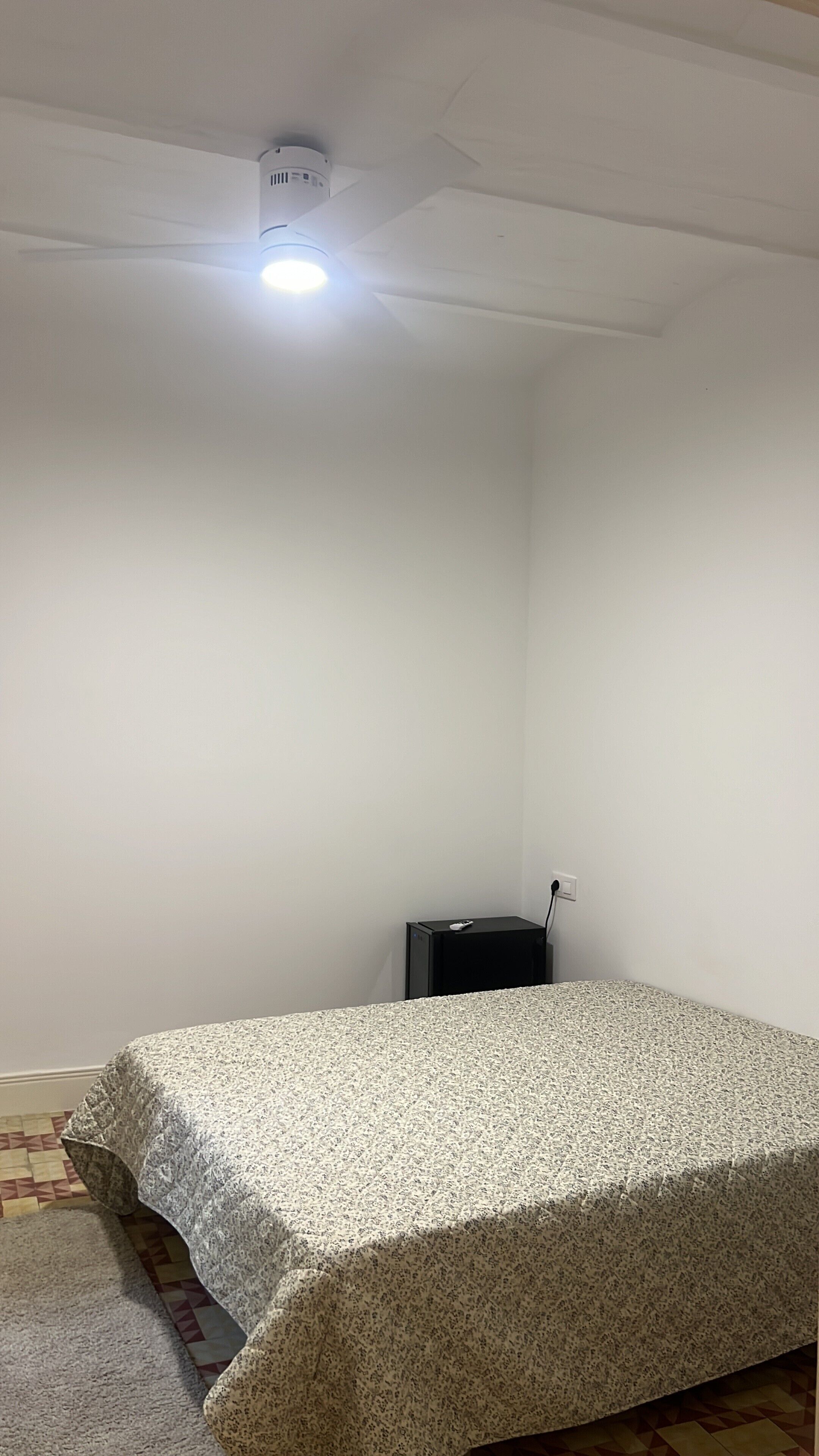 Et værelse med en seng, et lille sort bord og en loftlampe.