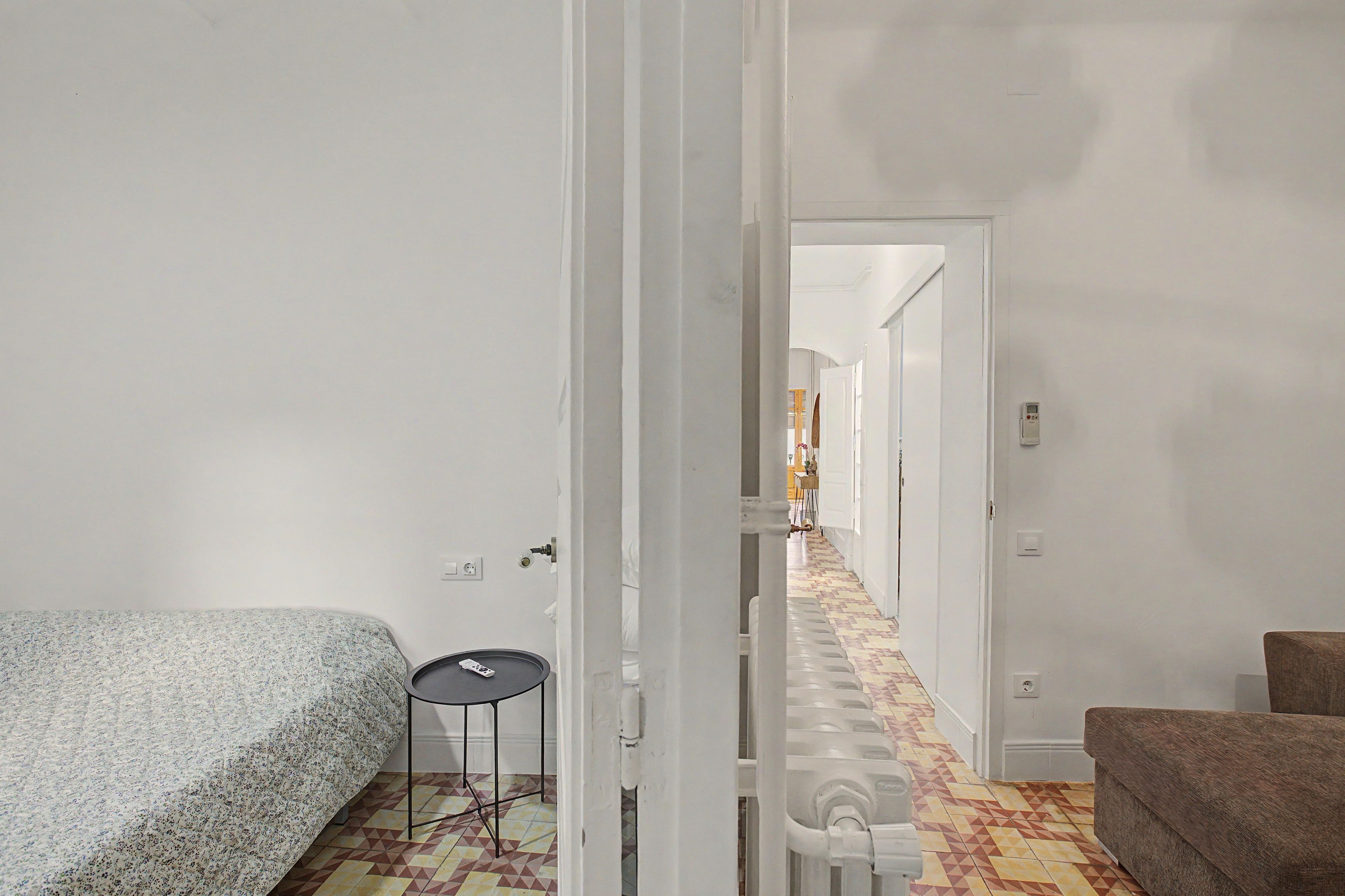 A hotel room with a bed, a small table, a radiator, and a chair.