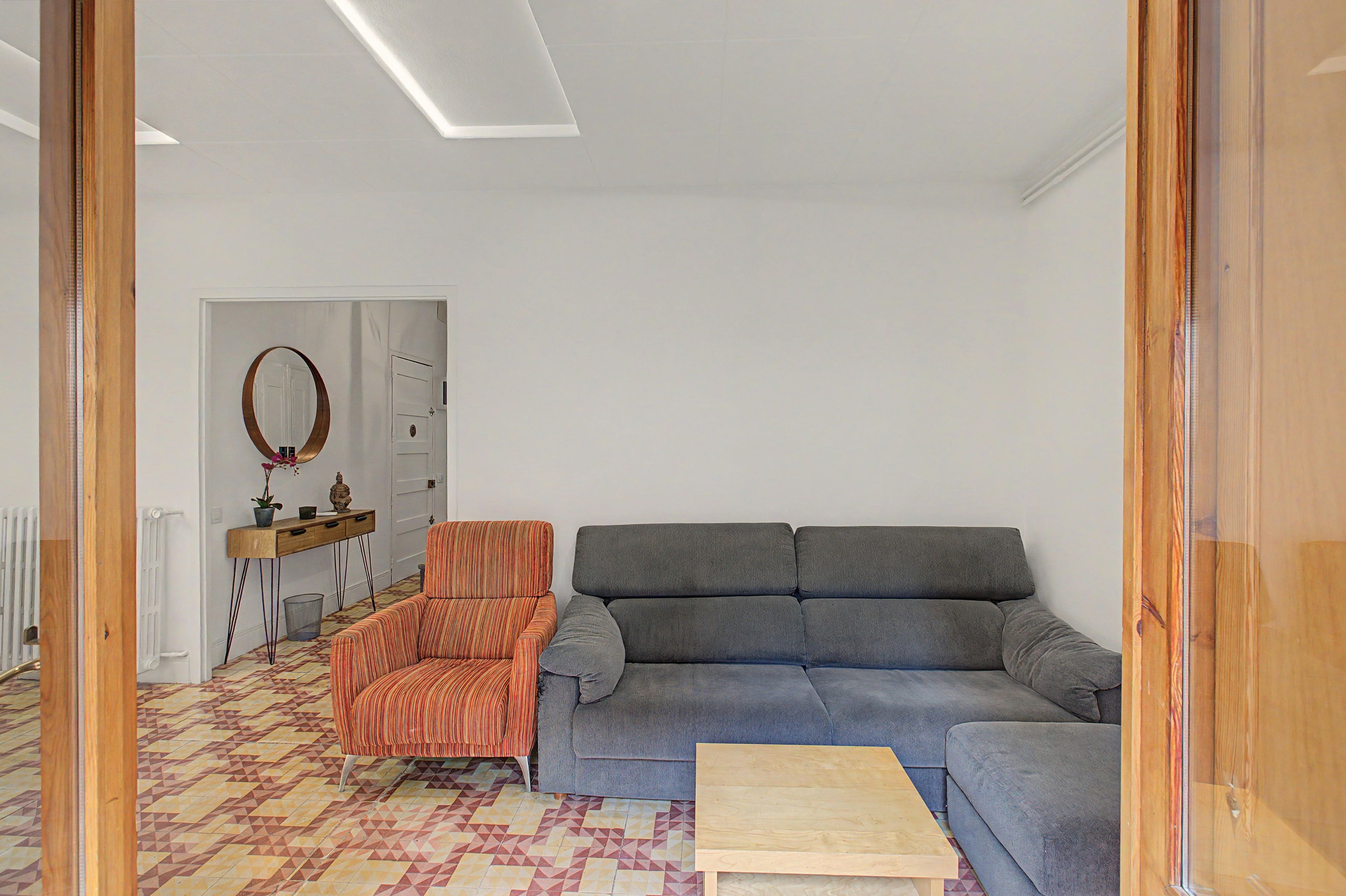A living room with a grey sofa, an orange-striped armchair, a wooden coffee table, and a patterned floor.
