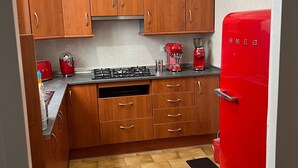 A kitchen with wooden cabinets, a red refrigerator, a clock, and a gas stove. - La Divina: Apartment with Balcony in the Heart of Figueres (Figueres)