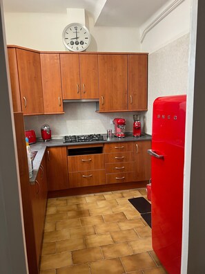 Une cuisine avec des meubles de rangement en bois, un réfrigérateur rouge, une horloge et une cuisinière à gaz.