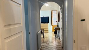 A hallway with patterned flooring, a television in the background, and a door on the left. - La Divina: Apartment with Balcony in the Heart of Figueres (Figueres)