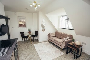 A modern living room with a sofa, a dining table with chairs, a kitchen area, and a large window. - Queensferry Collection - Residence 7 (Derby)
