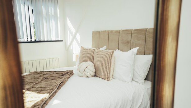 A bed with a beige headboard, white bedding, and a brown throw blanket. - Queensferry Collection - Residence 7 (Derby)