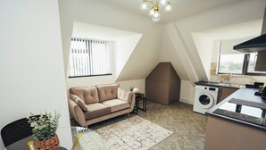 A compact living space with a sofa, a washing machine, a kitchenette, and a dining area with a glass table and chairs. - Queensferry Collection - Residence 7 (Derby)