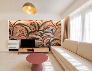 Ein modernes Wohnzimmer mit einer Couch, einem Flachbildfernseher, einem roten Couchtisch und einer Wand mit abstrakter Kunst.