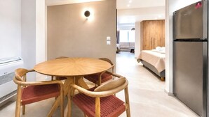 Habitación de hotel moderna con una mesa redonda de madera, cuatro sillas, una cama, armario empotrado y refrigerador.