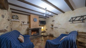 Ein rustikaler Raum mit Steinwänden, einem Kamin, zwei gestreiften Sofas und einem Fernseher.