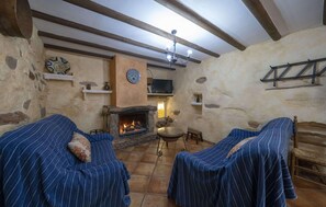 Ein rustikaler Raum mit Steinwänden, einem Kamin, zwei gestreiften Sofas und einem Fernseher.