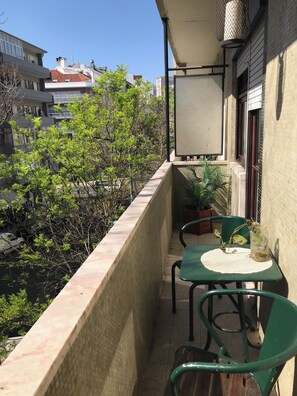 Ein Balkon mit Tisch und Stühlen, einem Blumentopf und Blick auf Häuser und Bäume.