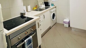 Ett kök med vita skåp, en spis, en mikrovågsugn, ett handfat och en tvättmaskin.