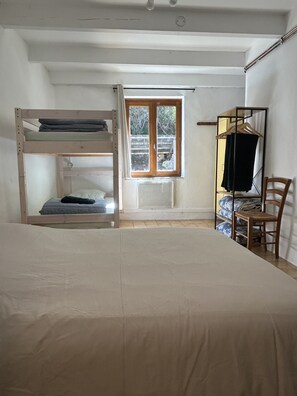 Une chambre avec un lit superposé, une fenêtre donnant sur un beau paysage, une chaise et un portant à vêtements.