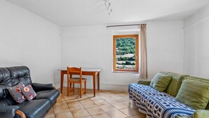 Une pièce comprenant un canapé en cuir noir, un canapé vert, une table à manger en bois avec une chaise, et une fenêtre donnant sur un paysage verdoyant.