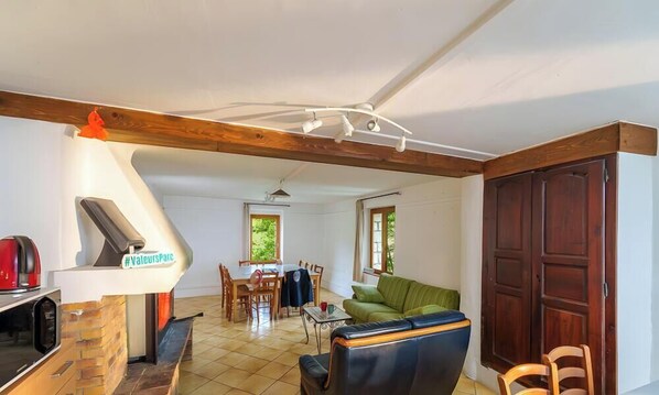 A living room with a fireplace, a dining area, and a large wooden door. - Room 'Chambre Jaune' with Mountain View, Shared Terrace and Shared Garden (Blieux)