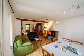 A living room with a green sofa, a dining table with chairs, a fireplace, and a kitchen area in the background. - Room 'Chambre Jaune' with Mountain View, Shared Terrace and Shared Garden (Blieux)