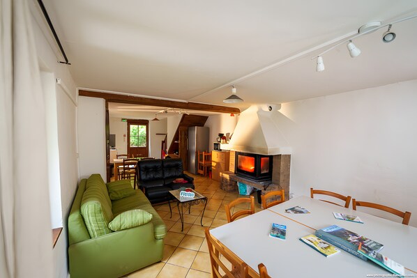 Un salon avec un canapé vert, une table à manger avec des chaises, une cheminée et, au fond, un coin cuisine.