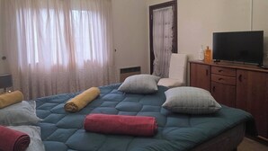 Ein Schlafzimmer mit Bett, Fernseher, Sessel und einer Deckenleuchte.