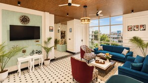 Una sala de estar moderna con un televisor de pantalla plana, un sillón rojo, un sofá azul y un amplio ventanal con vistas a la ciudad.