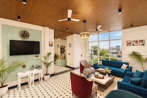 Ein modernes Wohnzimmer mit Flachbildfernseher, einem roten Sessel, einem blauen Sofa und einem großen Fenster mit Blick auf die Stadt.