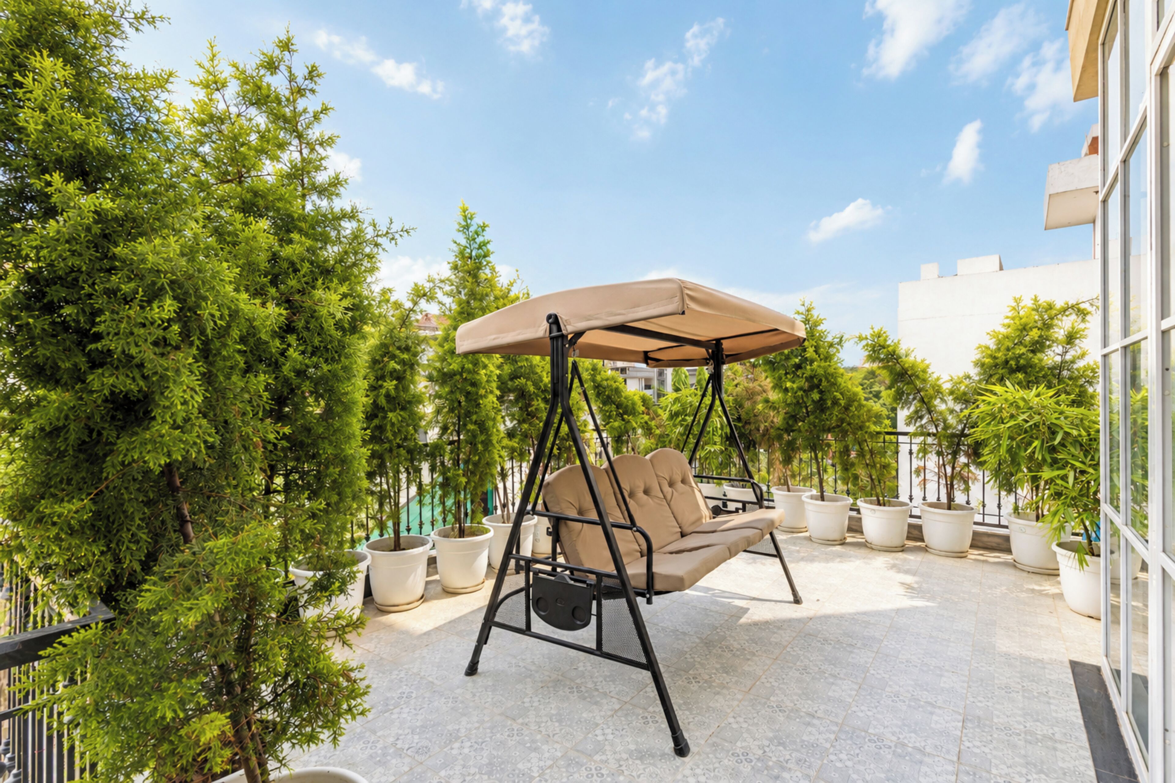 Un patio con una silla mecedora, plantas en macetas y un edificio al fondo.
