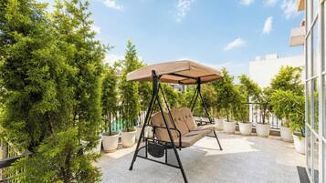 Un patio con una silla mecedora, plantas en macetas y un edificio al fondo.