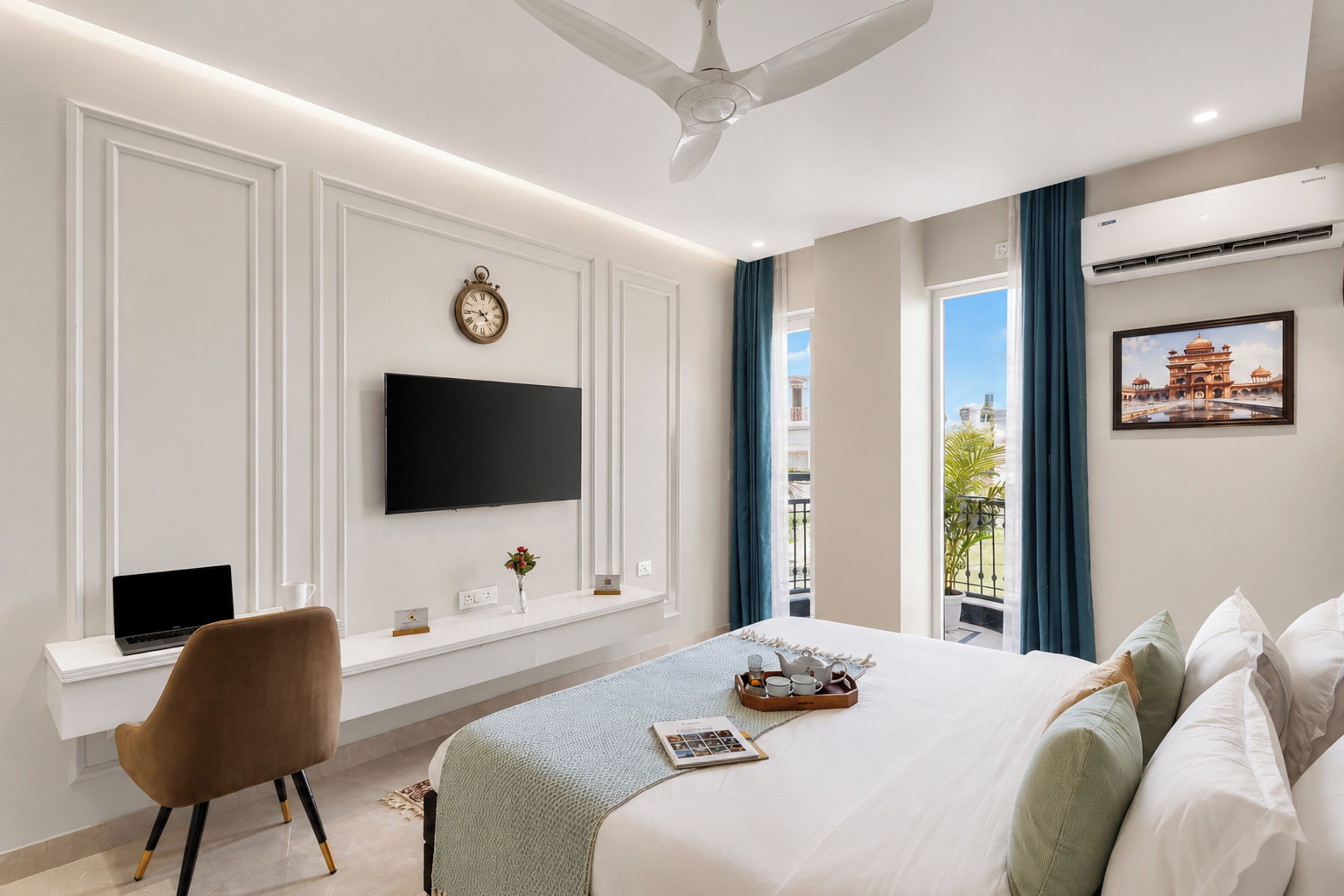 A modern hotel room with a bed, a desk with a laptop, a TV, a clock, and a window with a view.