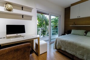A bedroom with a bed, a desk with a computer, a chair, and a window with a view of greenery. - Casa Serena | Oceanfront, Heated Pool, Jacuzzi & Fireplace (Florianópolis)