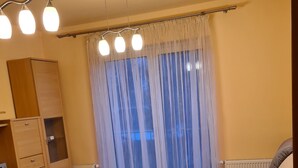A living room with a sofa, a wooden cabinet, a radiator, and a window with sheer curtains.