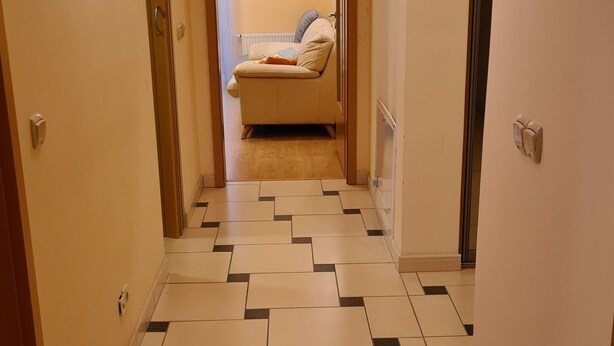 A hallway with patterned flooring, doors, and a bed in the background.