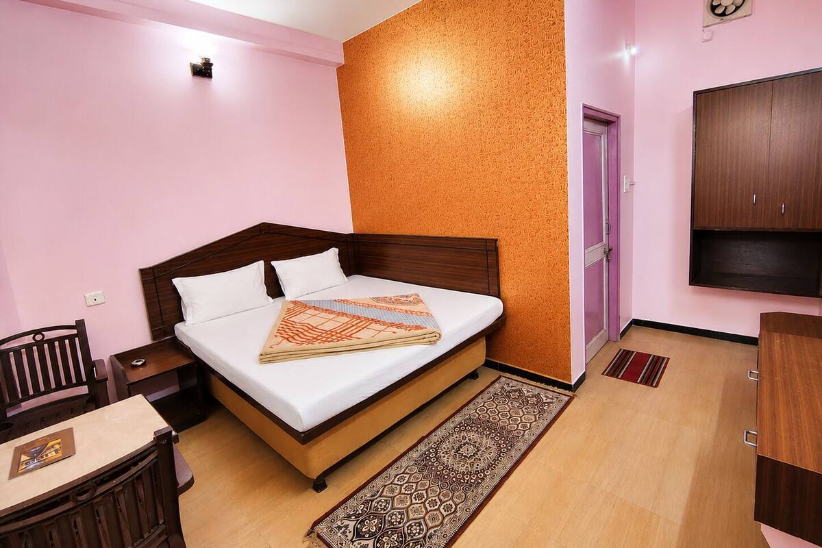 A bedroom with a bed, a desk, a chair, a wardrobe, and a television.