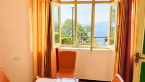 A room with a large window, two orange chairs, a wooden table, and a green door.