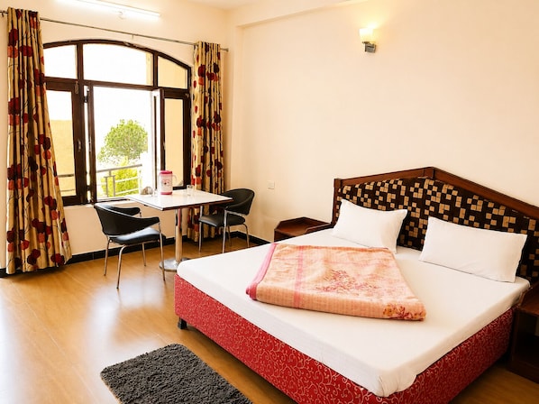 A hotel room with a bed, a desk, two chairs, a window with curtains, and a nightstand. - Hotel Hill Top Forest Palace (Jaiharikhal)