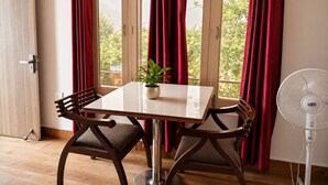A dining area with a table, chairs, a potted plant, and a standing fan.