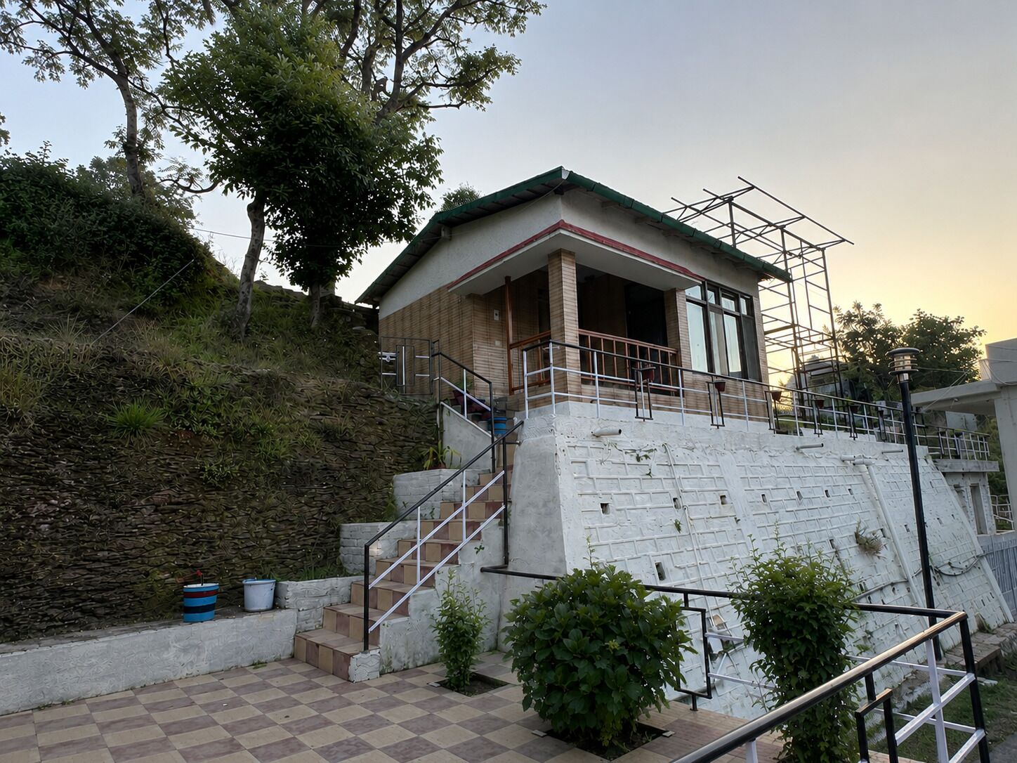 Um edifício com escadaria de pedra que leva a uma entrada coberta, rodeado por vegetação e um muro de pedra.
