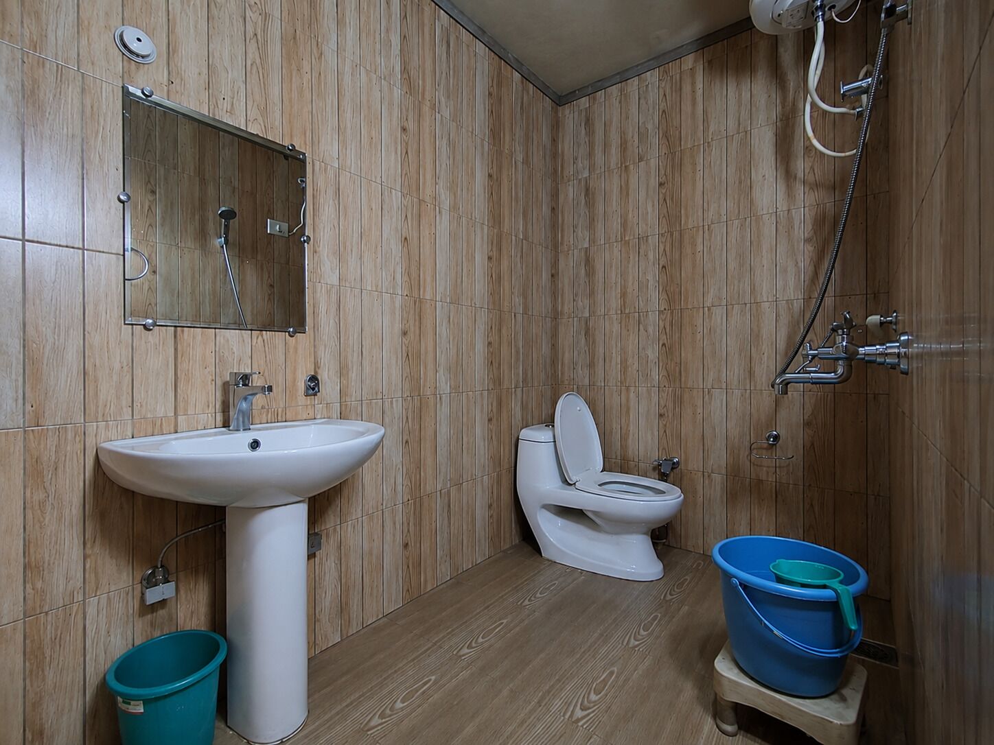 A bathroom with a wooden wall panel, a white sink, a toilet, and a shower.
