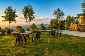 A patio with outdoor furniture, a stone wall, and a view of mountains. - Hotel Hill Top Forest Palace (Jaiharikhal)
