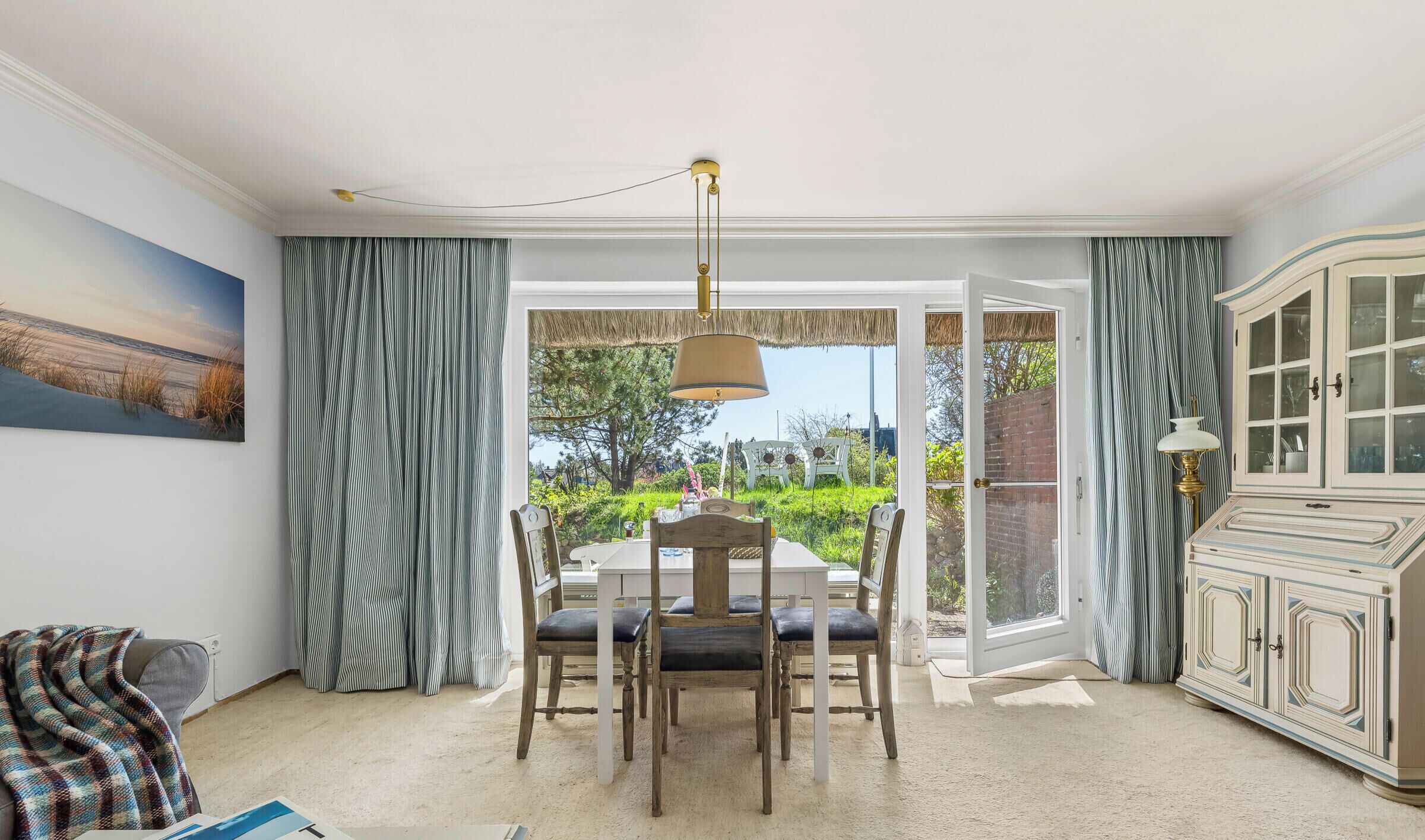 A dining area with a table and chairs, a chandelier, a cabinet, and a view through glass doors to an outdoor garden.
