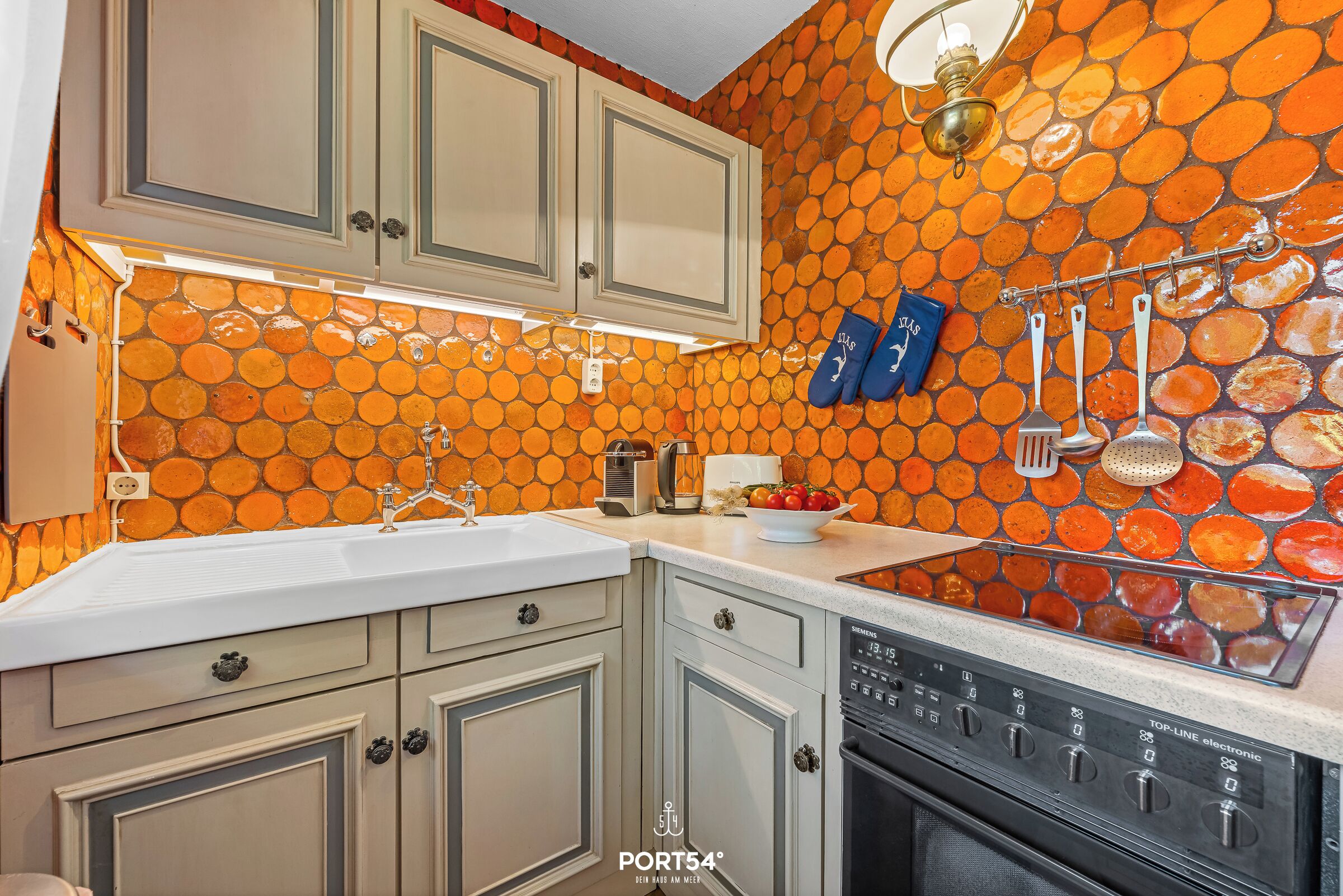 A kitchen with a unique orange mosaic backsplash, white cabinets, and a dishwasher.