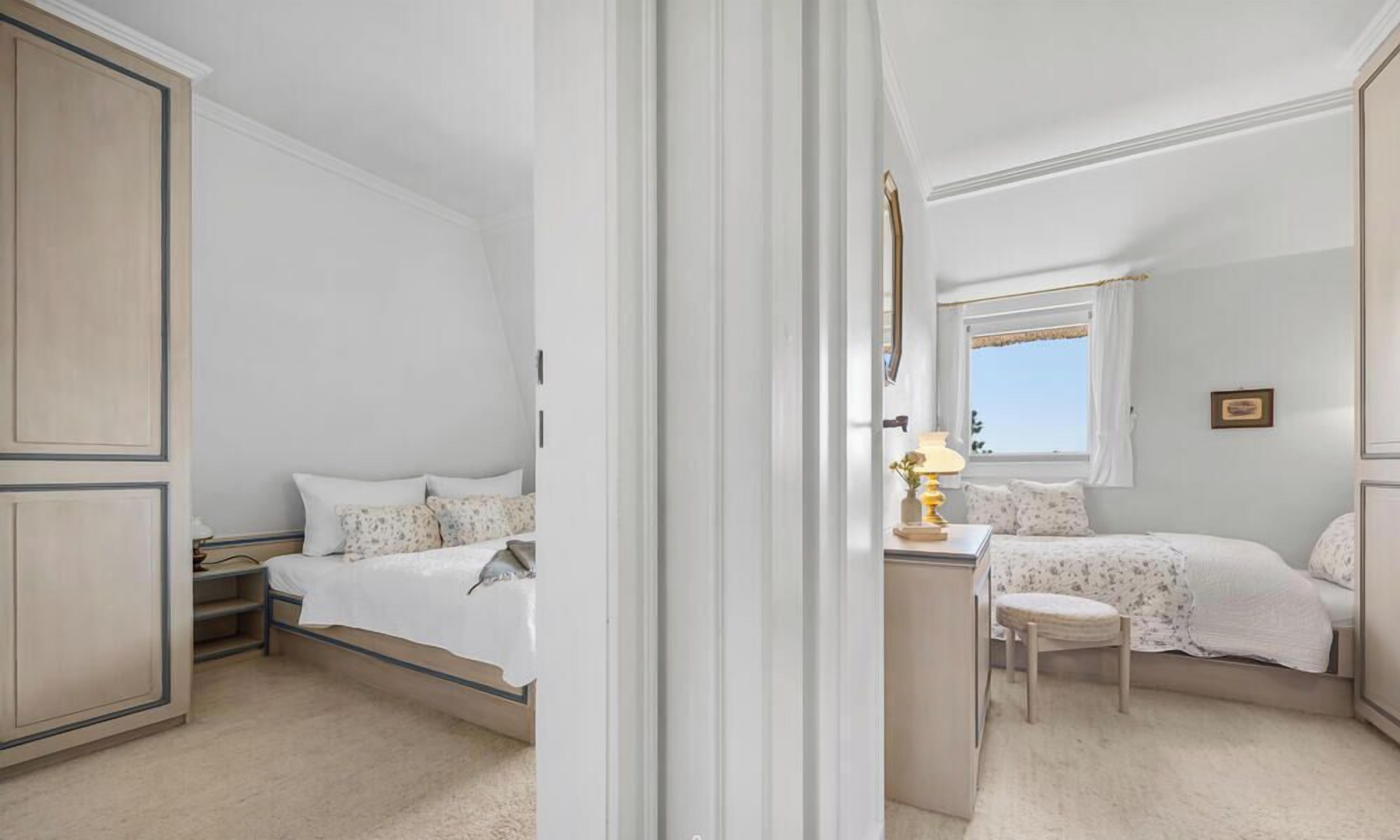 A bedroom with two beds, a bedside table, a chair, and a window.